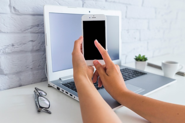 Bezpłatne zdjęcie ręka dotyka przenośnego ekranu przed laptopem nad białym biurkiem