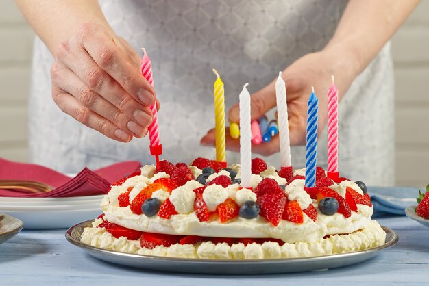 Ręka kobiety dodaje świeczki urodzinowe do domowego ciasta truskawkowego ciasta truskawkowego i świeczek urodzinowych