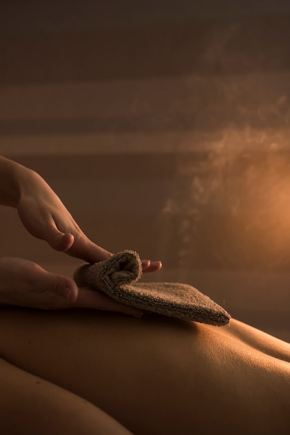 Ręka kosmetyczka masuje plecy kobiety z gorącym ręcznikiem w spa