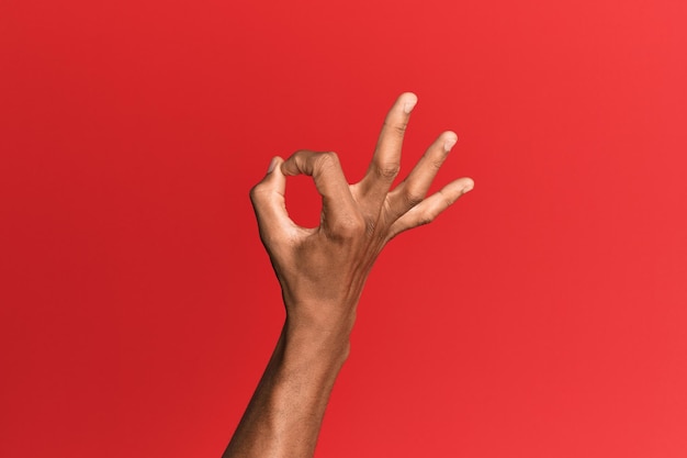 Bezpłatne zdjęcie ręka latynoskiego mężczyzny na czerwonym, odosobnionym tle gestykuluje wyrażenie zgody, robiąc dobrze symbol palcami