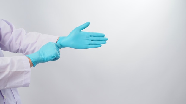 Ręka lekarza ciągnie niebieskie lateksowe rękawiczki na białym tle