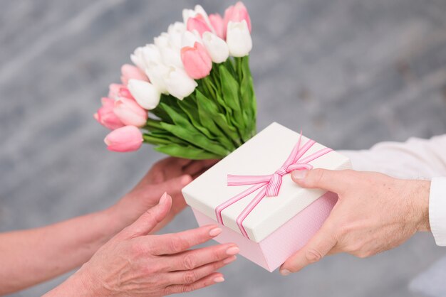 Ręka mężczyzny dając prezent urodzinowy i bukiet kwiatów tulipanów do jego żony