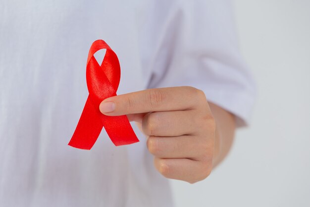Ręka młodej kobiety trzymająca czerwoną wstążkę z rakiem piersi i świadomością AIDS