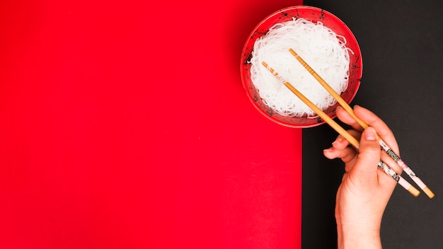 Bezpłatne zdjęcie ręka osoby używa pałeczek do zbierania smacznych makaronów na parze w misce nad podwójnym stołem