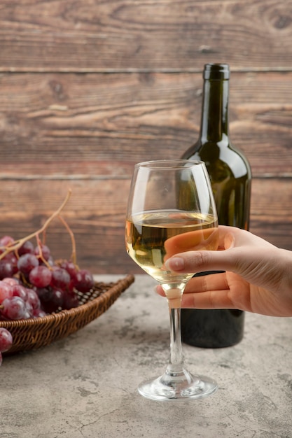 Ręka trzyma kieliszek białego wina na marmurowym stole.
