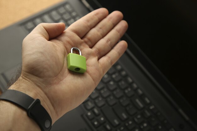 Ręka trzyma zieloną kłódkę z laptopem w tle. Koncepcja bezpieczeństwa cybernetycznego.