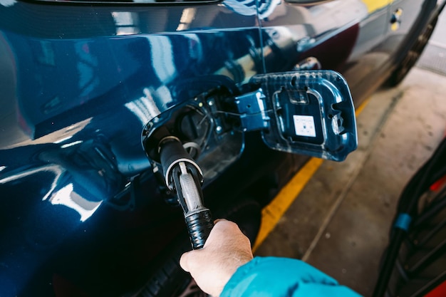 Ręka trzymająca wąż podłączony do samochodu wykonanego z paliwa lpg (gaz płynny) na stacji benzynowej w metalicznym niebieskim samochodzie. tankowanie, stacja benzynowa, ekologia, transport i koncepcja eko.