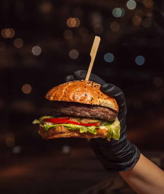 Ręka w burger rękawiczkach trzyma wołowina hamburger w czarnym tle