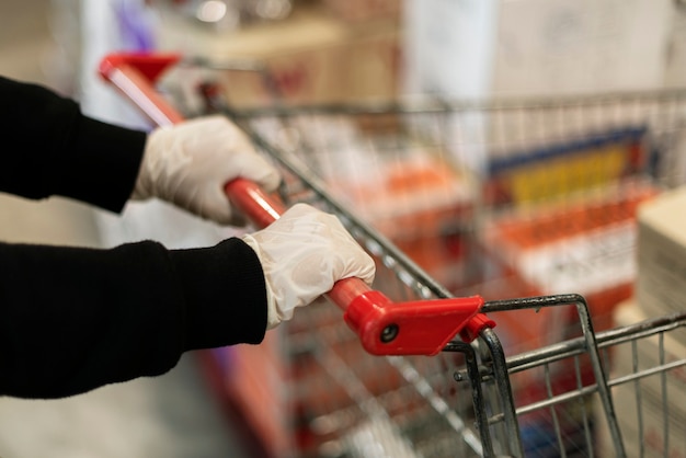Ręka w lateksowej rękawiczce podczas pchania wózka na zakupy, aby zapobiec zakażeniu koronawirusem