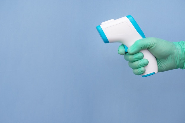 Ręka w rękawiczce pracownika służby zdrowia trzymającego termometr na niebieskim tle