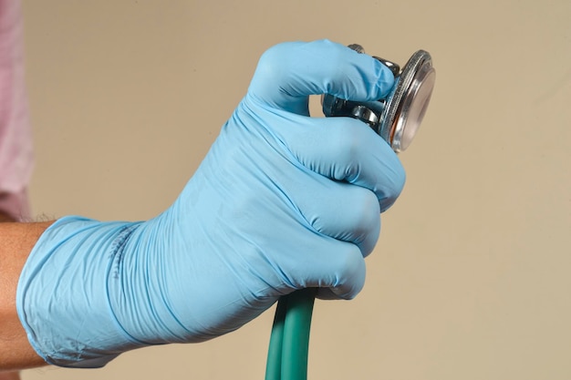 Ręka w rękawiczkach ochronnych trzymająca przedmiot medyczny na jasnobrązowym tle