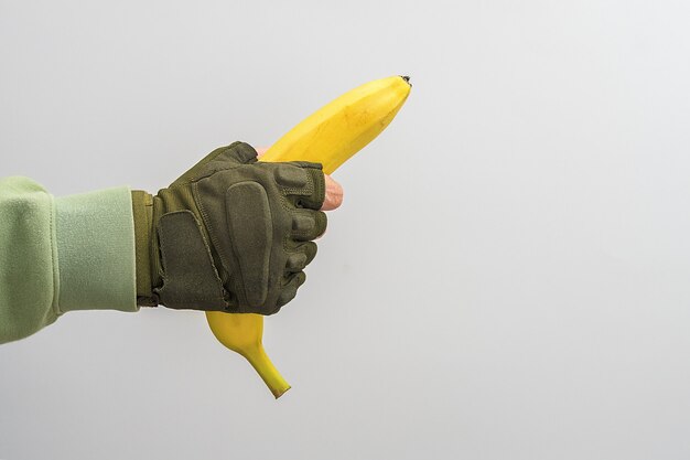 Ręka wojskowa mężczyzny trzyma banana na szarym tle.