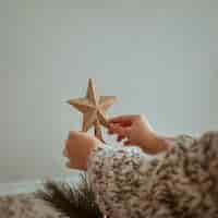 Bezpłatne zdjęcie ręki trzyma złotą wierzchołek gwiazdę dla choinki