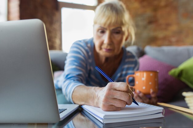 Robienie notatek podczas lekcji. Starsza kobieta uczy się w domu, pobiera kursy online