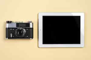 Bezpłatne zdjęcie rocznik kamera blisko cyfrowej pastylki z pustym czarnym ekranu pokazem na beżowym tle