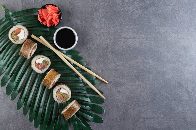 Roladki sushi, sos sojowy, wasabi i marynowany imbir na kamiennym tle.
