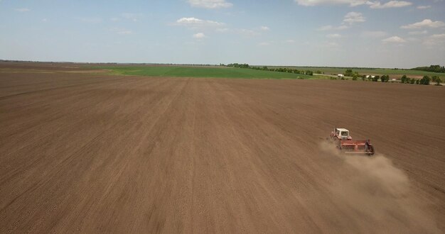 Rolnik ciągnikiem przygotowujący pole z kultywatorem przedsiewnym w ramach czynności przedsiewnych w okresie wczesnowiosennym prac rolniczych na polach uprawnych Zdjęcie drona