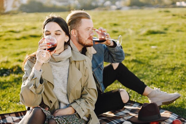 Bezpłatne zdjęcie romantyczna para w modne ubrania, siedząc na przyrodzie na dywanie piknikowym. mężczyzna ubrany w kurtkę i płaszcz damski