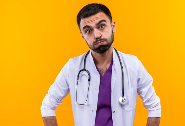 Rozczarować młody mężczyzna lekarz ubrany w stetoskop medycznej sukni na na białym tle żółtej ścianie