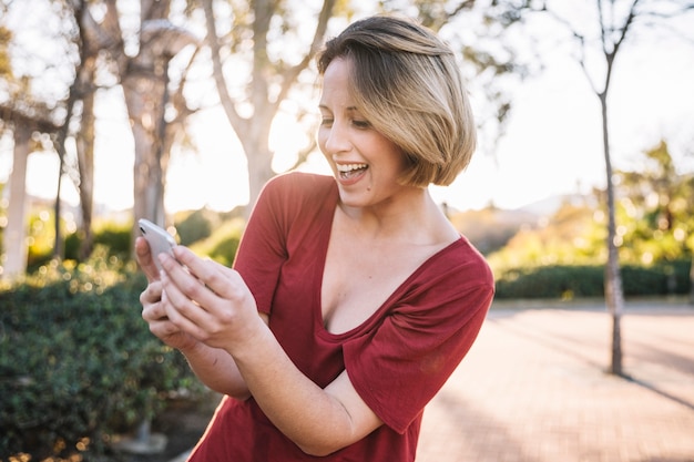 Roześmiana kobieta wyszukuje smartphone na parkowej alei