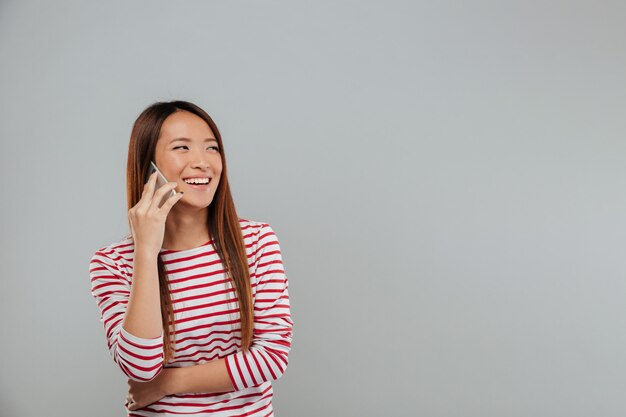 Roześmiana młoda azjatykcia kobieta opowiada telefonem
