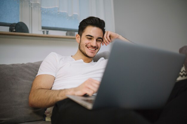 Roześmiany mężczyzna używa laptop na kanapie