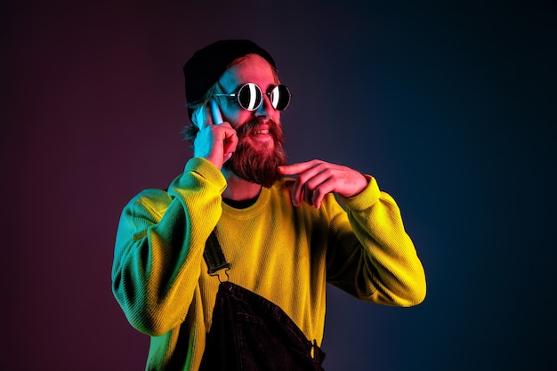 Rozmowa przez telefon w okularach przeciwsłonecznych. Portret mężczyzny rasy kaukaskiej na tle gradientu studio w świetle neonu. Piękny męski model w stylu hipster. Pojęcie ludzkich emocji, wyraz twarzy, sprzedaż, reklama.