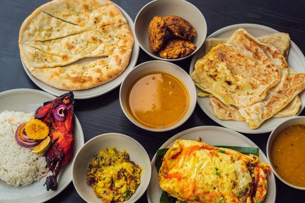 Różne indyjskie jedzenie na ciemnym tle drewnianych. dania i przekąski kuchni indyjskiej. curry, kurczak maślany, ryż, soczewica, paneer, samosa, naan, chutney, przyprawy. miski i talerze z indyjskim jedzeniem