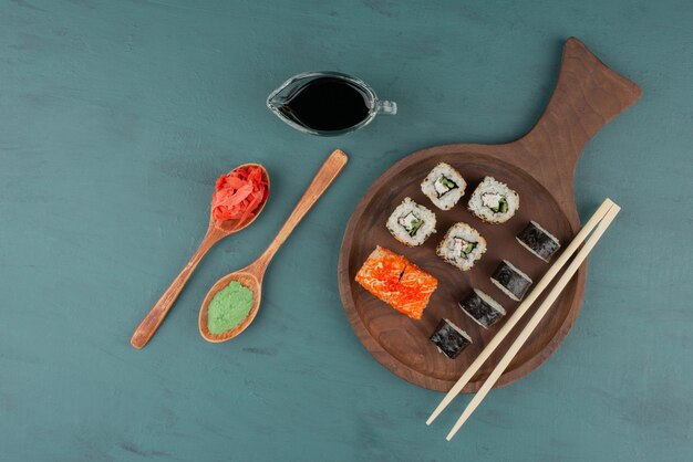 Różne rodzaje rolek sushi z marynowanym imbirem, wasabi i sosem sojowym na niebieskim stole.