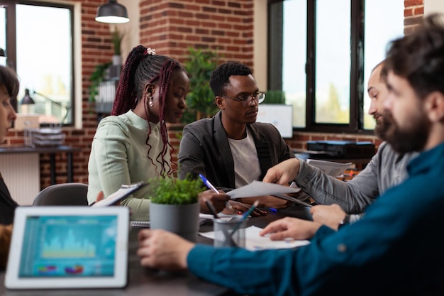 Różnorodni biznesmeni pracujący nad projektem marketingowym analizującym strategię finansową w biurze startupowym. Wieloetniczny zespół omawiający współpracę biznesową w zakresie planowania obrotów firmy. Firmowe miejsce pracy