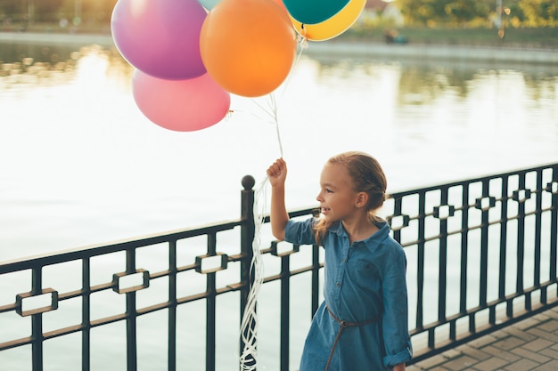 Rozochocona dziewczyna trzyma kolorowych balony i dziecięcą walizkę