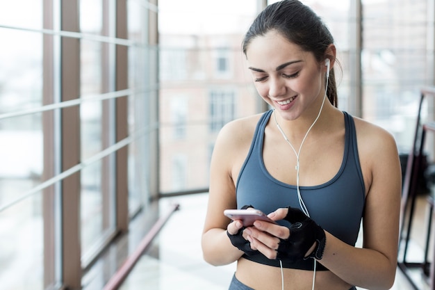 Rozochocona kobieta używa smartphone przy okno w gym