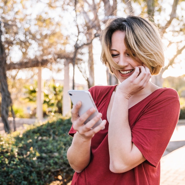 Rozochocona kobieta używa smartphone w pięknym parku