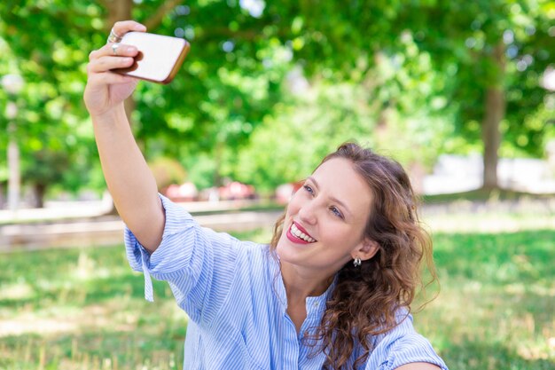 Rozochocona młoda kobieta pozuje dla selfie na smartphone