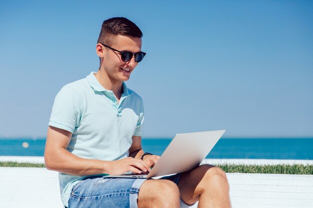 Rozochocony facet w okularach przeciwsłonecznych pracuje na laptopie, pisać na maszynie, wyszukujący strony internetowe