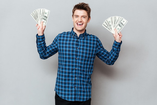 Bezpłatne zdjęcie rozochocony mężczyzna stoi nad popielatym ściennym mienie pieniądze.