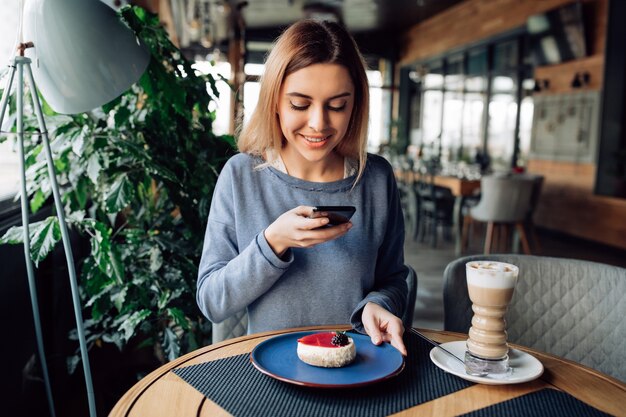 Rozochocony nicegirl bierze fotografię smakowity tort na telefonie komórkowym, wydaje czas przy kawiarnią