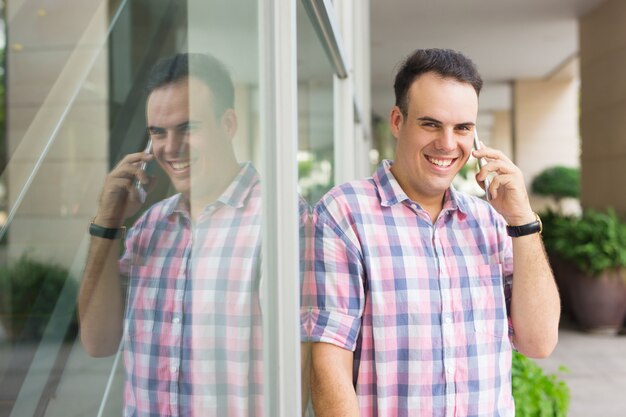 Rozochocony optymistyczny młody człowiek dzwoni na telefonie komórkowym