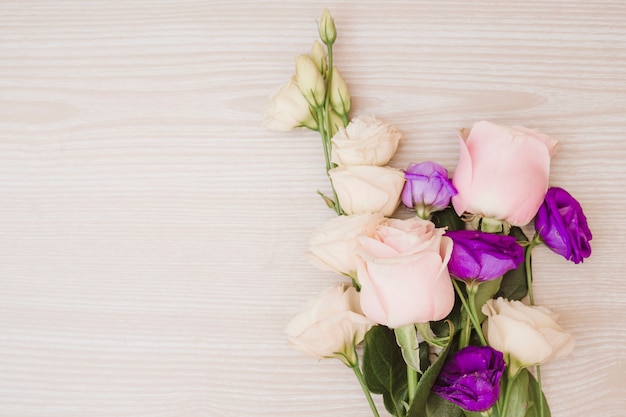 Różowe róże i purpurowy eustoma kwitną na drewnianym biurku
