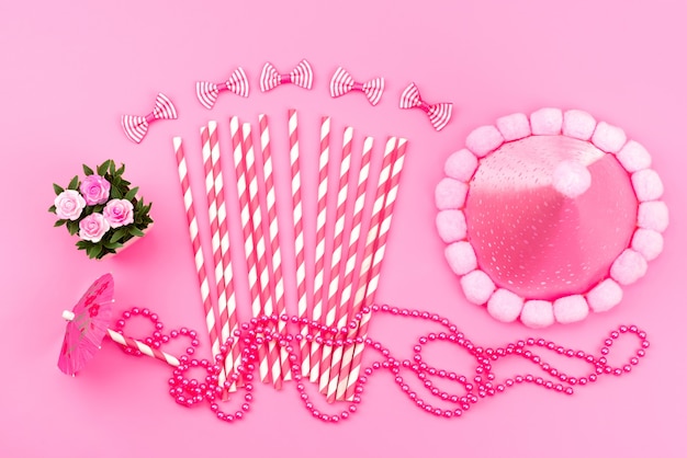 Różowo-białe cukierki w sztyfcie z widokiem z góry wraz z uroczą różową czapką urodzinową, kokardkami na różowym, urodzinowym kolorze
