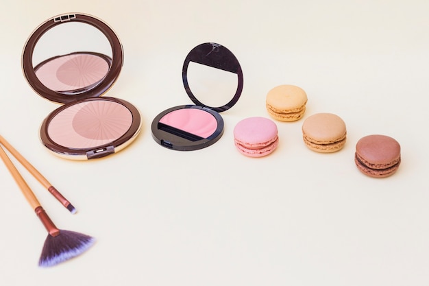 Bezpłatne zdjęcie różowy i beżowy blusher i makeup muśnięcie z macaroons na barwionym tle