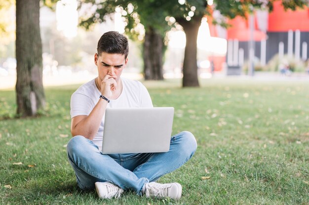 Rozważny młody człowiek używa laptop w ogródzie