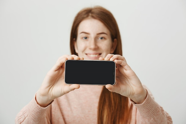 Ruda nastolatka pokazuje wyświetlacz smartfona