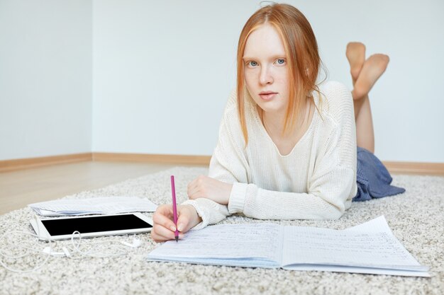 Bezpłatne zdjęcie rude kobiety leżącej na podłodze z notebookiem i tabletem