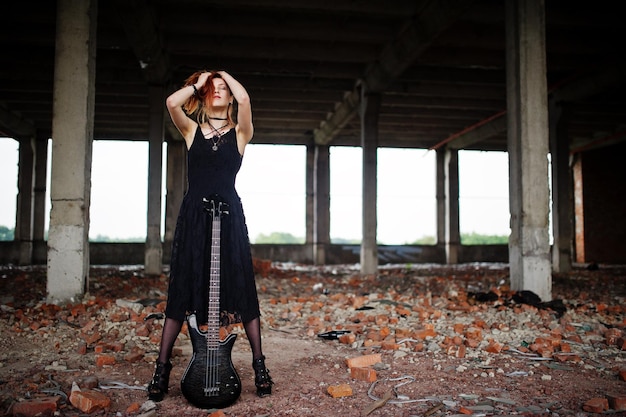 Bezpłatne zdjęcie rudowłosa dziewczyna punkowa nosi na czarno z gitarą basową w opuszczonym miejscu portret gotyckiej kobiety muzyk