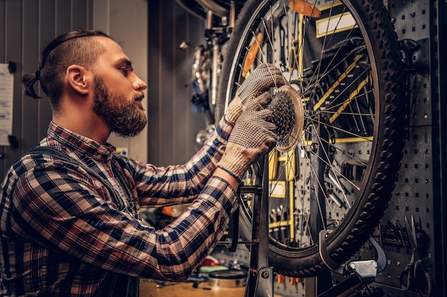 Rudowłosy, brodaty mechanik zdejmujący tylną kasetę rowerową w warsztacie.