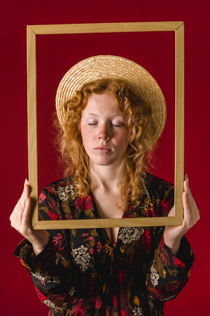 Bezpłatne zdjęcie rudzielec młodej kobiety mienia rama z zamkniętymi oczami