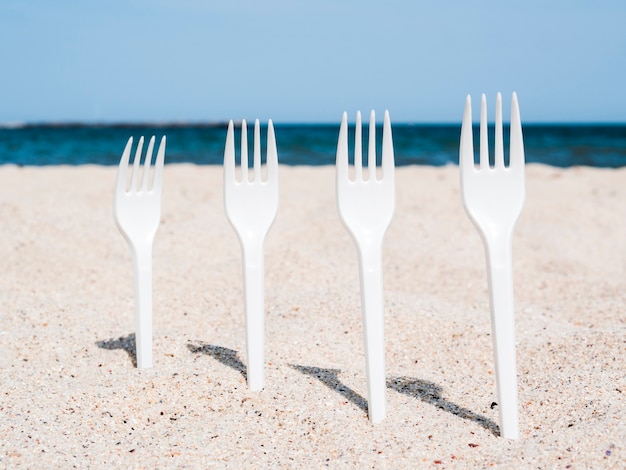 Bezpłatne zdjęcie rząd białych plastikowych widelców utknął w piasku na plaży