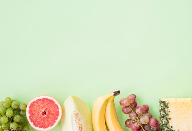 Rząd winogron; grejpfrut; muskmelon; banan; winogrona i ananas na pastelowym tle