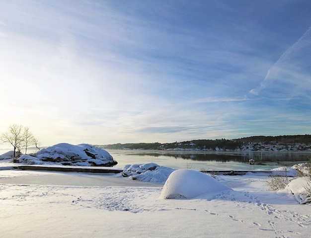 Rzeka otoczona skałami i domami pokrytymi śniegiem w słońcu w Larvik w Norwegii